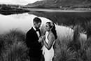 bride and groom lovingly standing in the middle of tall grass and lake- Queenstown Wedding