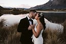 bride and groom kissing in the middle of tall grass and a beautiful lake view- Queenstown Wedding