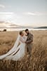 bride and groom standing in the middle of tall grass as the wind blows towards them- Taupo Wedding