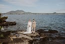 bride and groom standing in the middle of rocky edge of the sea- Taupo Wedding