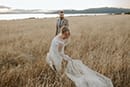 bride and groom in the middle of tall grass and wind blowing towards them- Taupo Wedding